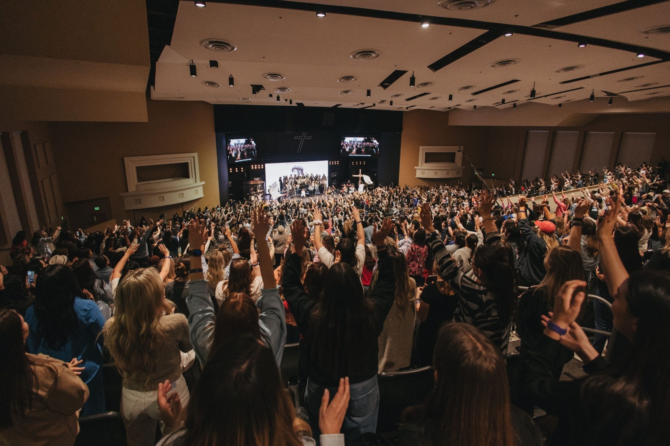 Wide angle image of attendees worshiping with arms raised